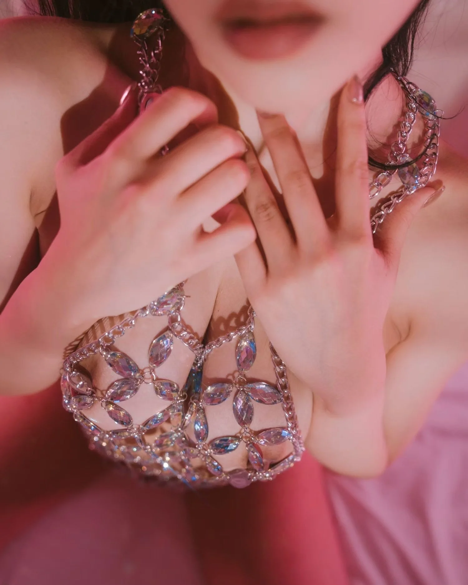 Close-up of a woman wearing large, sparkly jewelry and touching her neck, with soft pink lighting.