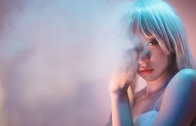 A woman with light-colored hair holds a cigarette near her face, with smoke partially obscuring her features in a moody, atmospheric setting.