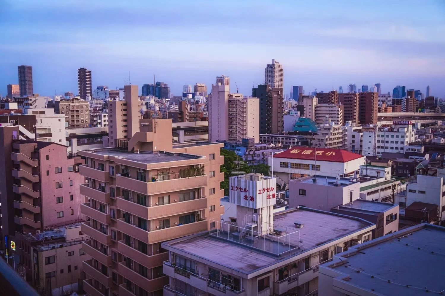 City skyline with numerous high-rise buildings and a pink apartment complex in the foreground, under a blue sky.