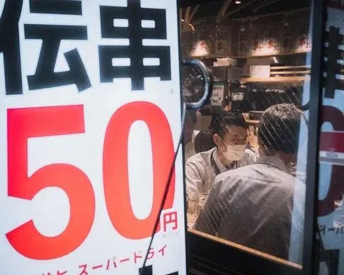 An outdoor street scene featuring two men enjoying a meal, captured through the reflection of a window.