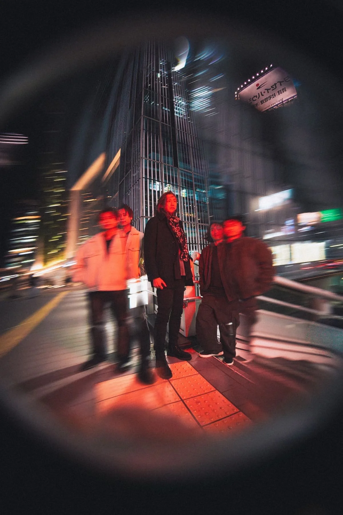 Nighttime city street scene with a group of five people waiting at a crosswalk, illuminated by neon city lights with a tall glass building in the background and a large billboard in the sky.