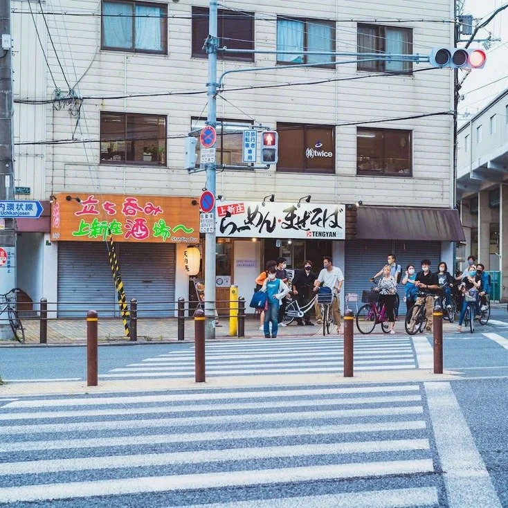 People crossing the street while riding bicycles in front of a colorful shop in Osaka, captured during slow travel in the city.
