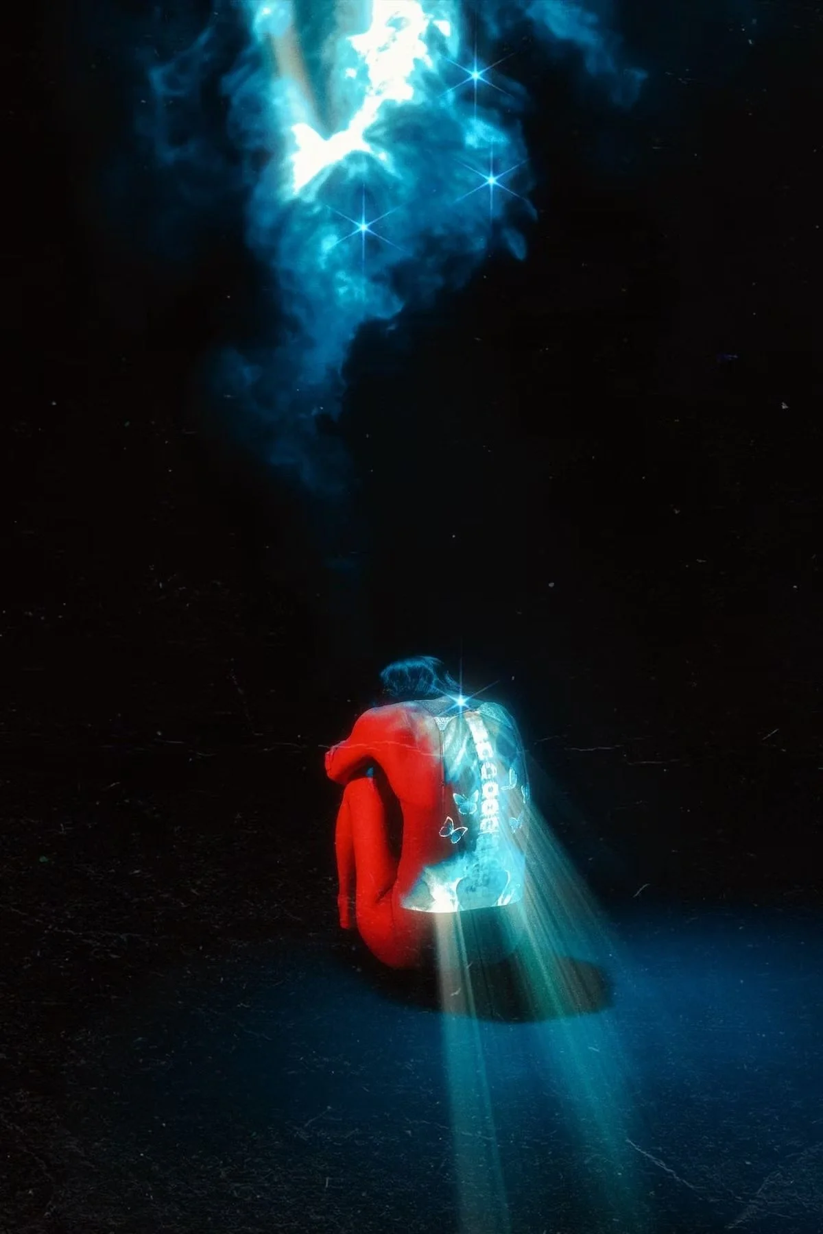 A person with short hair, wearing a red jacket and a backpack, sitting on the ground with their head down in a dark space, illuminated by a blue light. There is a blue cloud and star-like shapes in the sky above them, creating a celestial or dreamlik