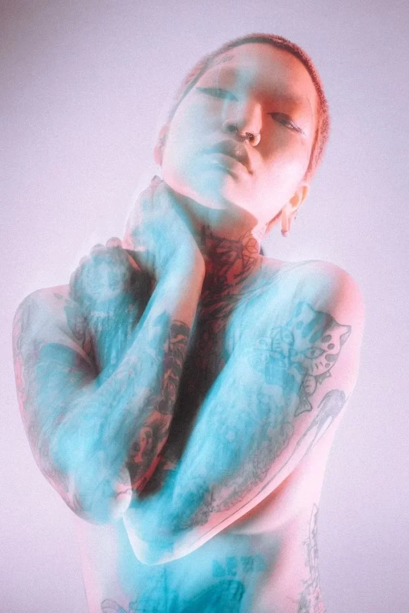A person stands amidst soft blue and pink smoke, creating an ethereal, artistic portrait. The dynamic color lighting and blurred movement add to the dreamlike atmosphere.