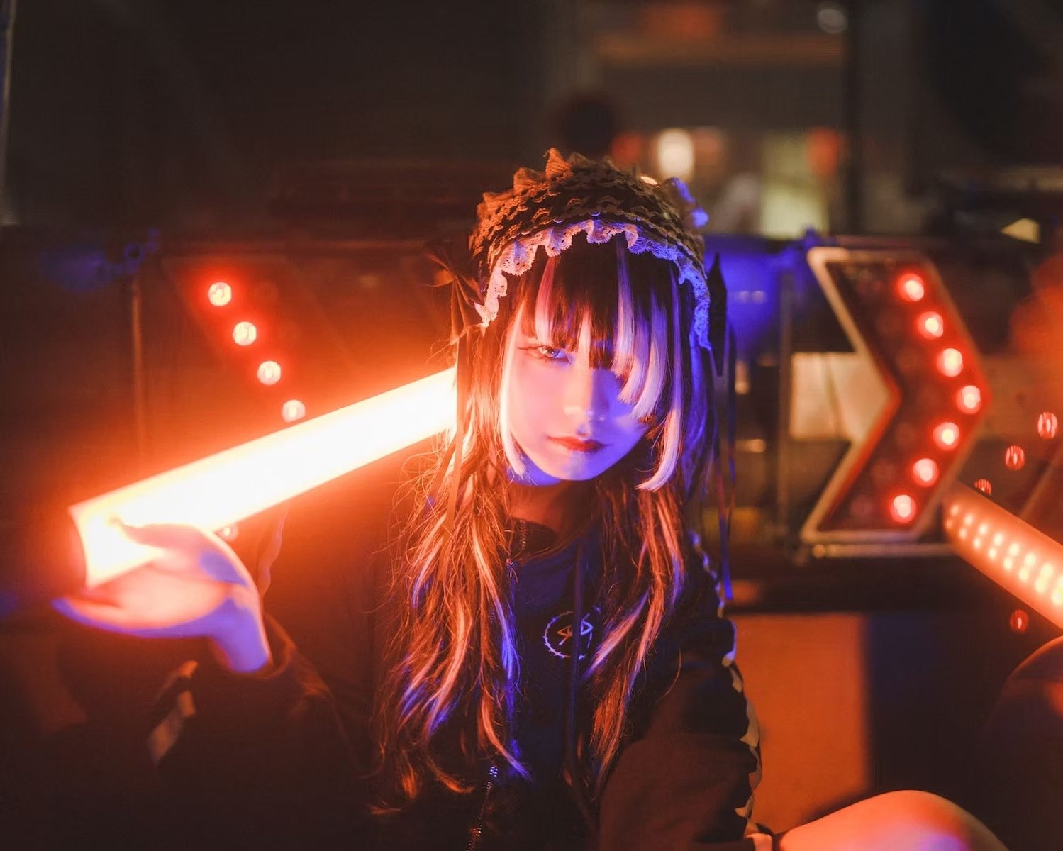 A young woman with long hair, wearing a bonnet, in a dimly lit environment with neon and LED lights, holding a glowing light bar, with colorful lights and industrial background. Captured by portrait photographer Deniz Demir.