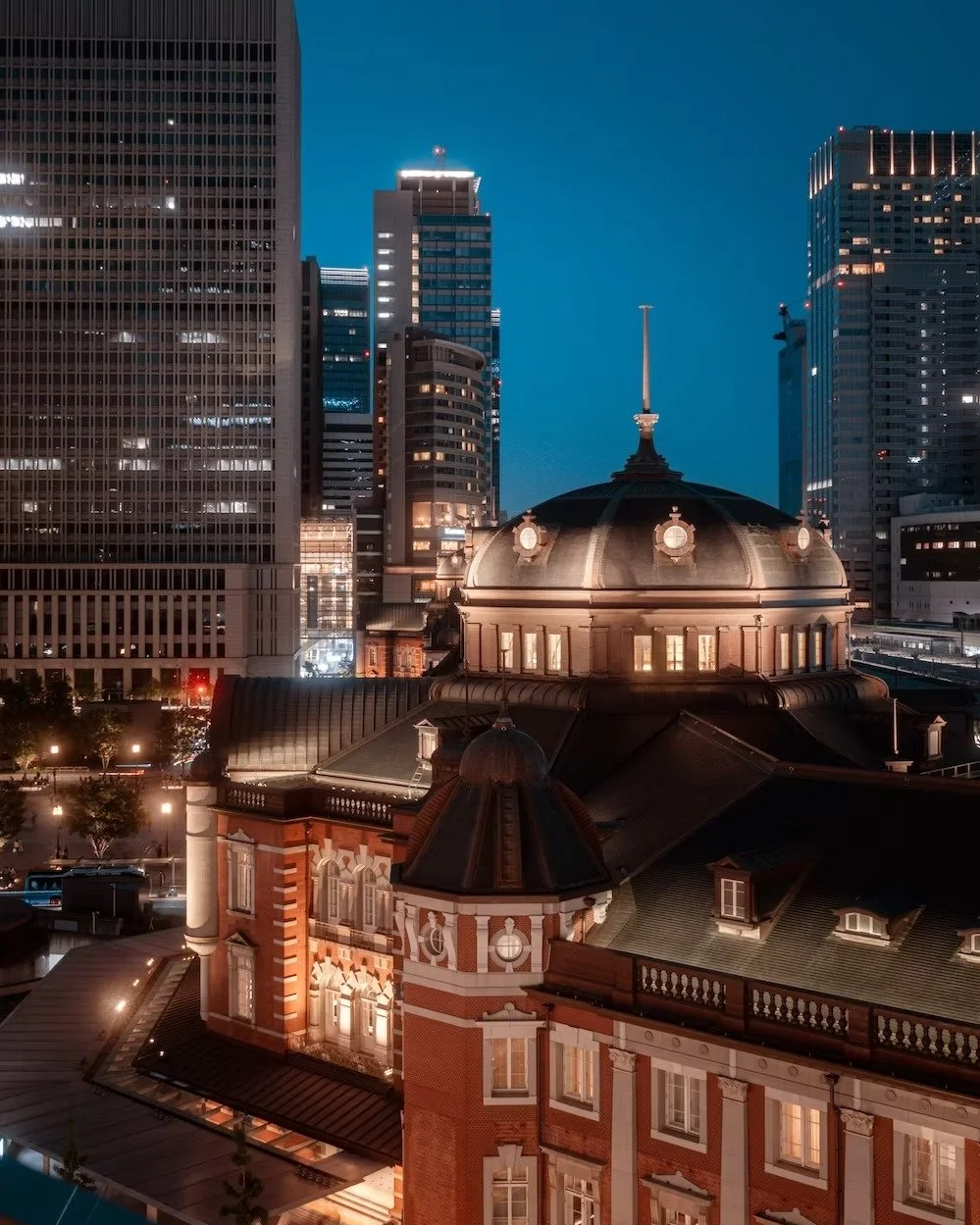 Nighttime cityscape showing historic building with a dome and spire surrounded by modern skyscrapers.