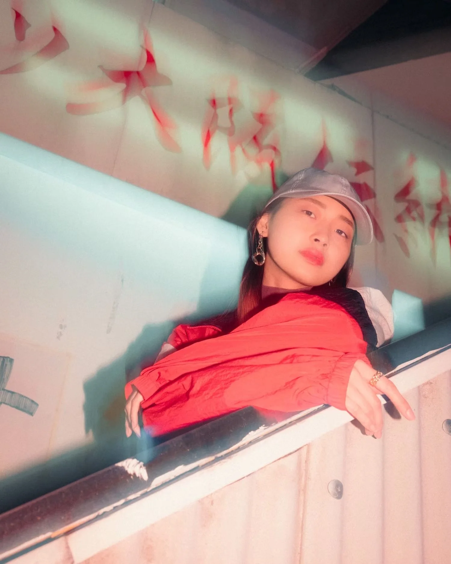 A Japanese woman with earrings and a cap taking a selfie in front of a colorful wall art installation.