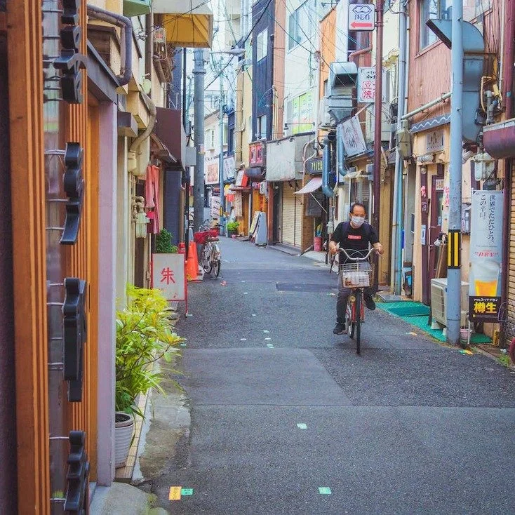 Man cycling across a colorful street in Osaka, with a prominent sign in the background, during slow travel.