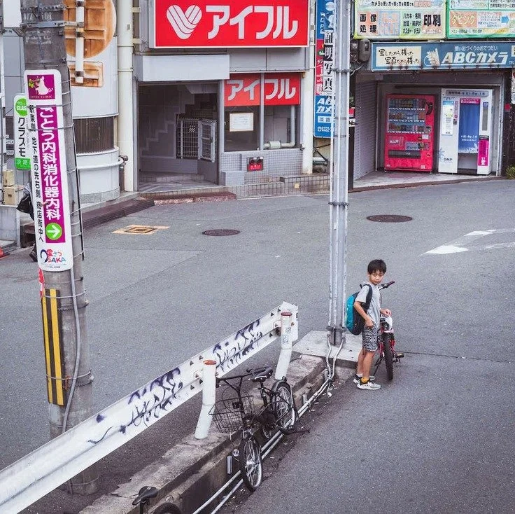 A child on a bicycle near bright advertisements in Osaka, captured while doing slow travel through the city.