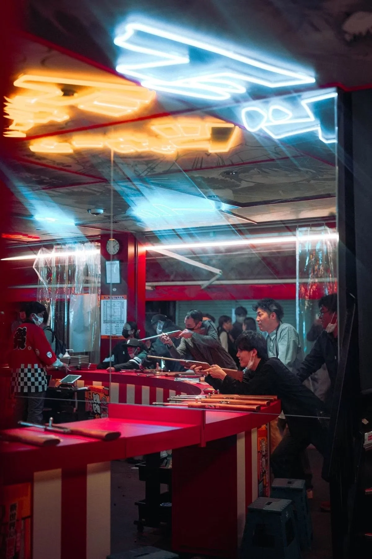 People gathered at a sushi restaurant with neon signs, some wearing masks, some ordering and serving. Osaka night scenes.