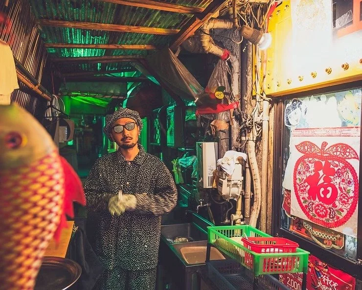 A man in a polka-dot outfit standing in a narrow alley in Kabukicho, surrounded by colorful walls and objects.