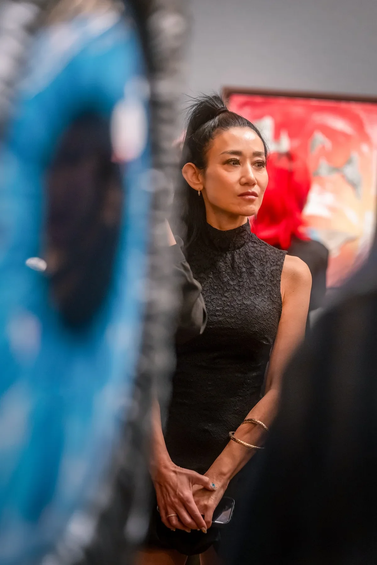 August Vilella
---
Candid editorial portrait of a woman wearing a black lace dress at August Vilella's art exhibition, photographed against a colourful gallery backdrop with soft foreground blur.