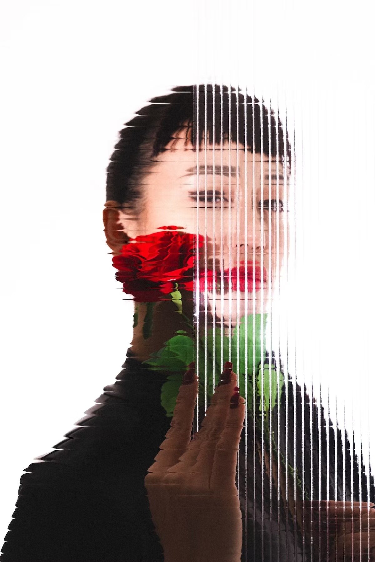 A woman with dark hair and makeup holding a bouquet of red roses behind a vertically striped glass or plastic surface.