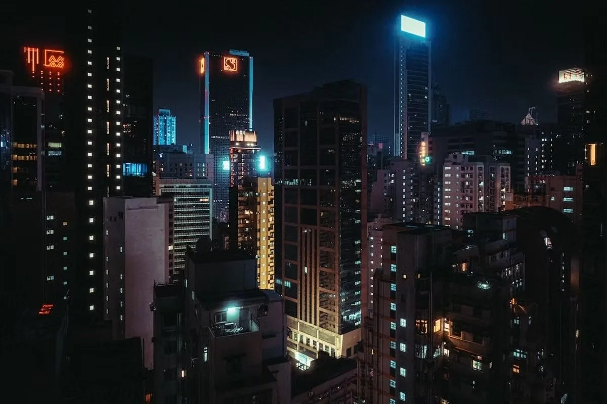 Nighttime cityscape with illuminated skyscrapers and buildings in a densely packed downtown area.