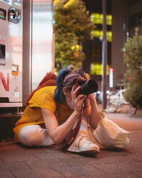 A person crouching to take a photo during the Tekumi Photowalks street photography workshop, capturing Tokyo's night scene.