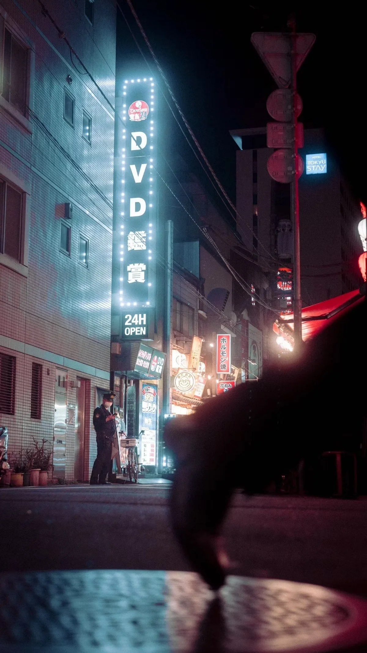Shimbashi Tokyo at night photographed by Tokyo street photographer Deniz Demir with a policeman in the background and a salaryman foot in the foreground.