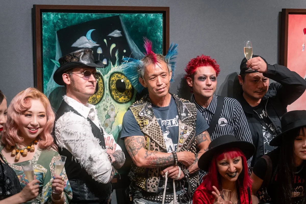 August Vilella
---
A group of exhibition guests pose together in front of August Vilella's surrealist owl-like creature painting, combining contemporary art, personal style, and documentary event photography.