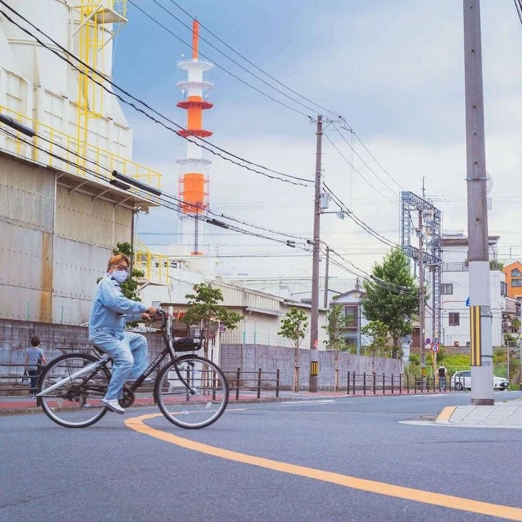 A man riding a bicycle along the streets of Osaka with power lines in the background, captured during slow travel.