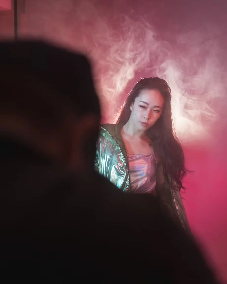 A model poses under green and red lighting while a soft mist creates a dynamic and vibrant atmosphere. The contrasting colors highlight her features and enhance the overall visual effect, giving the shot an intense, cinematic feel.