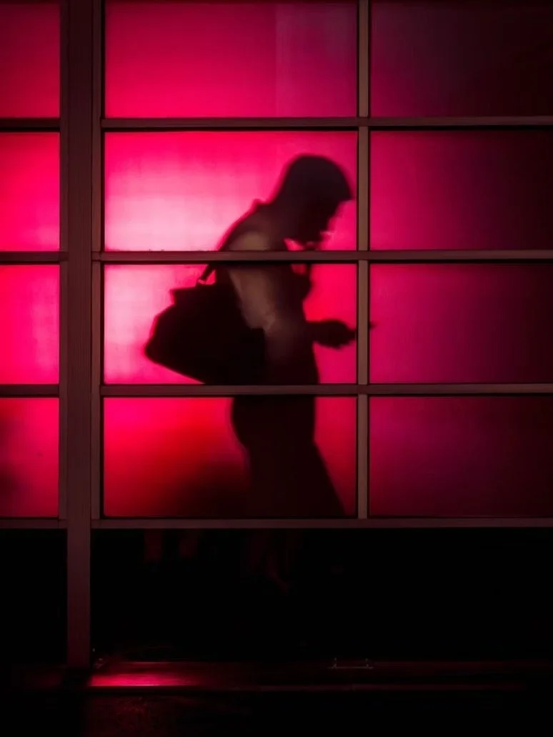 Silhouette of a person standing behind a glass window with pink lighting.