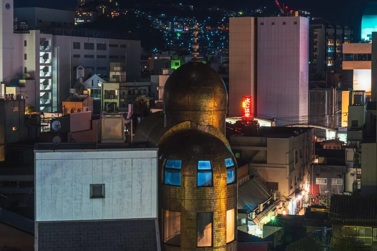 Nighttime cityscape with illuminated buildings, glowing signs, and a golden-domed building in the foreground.