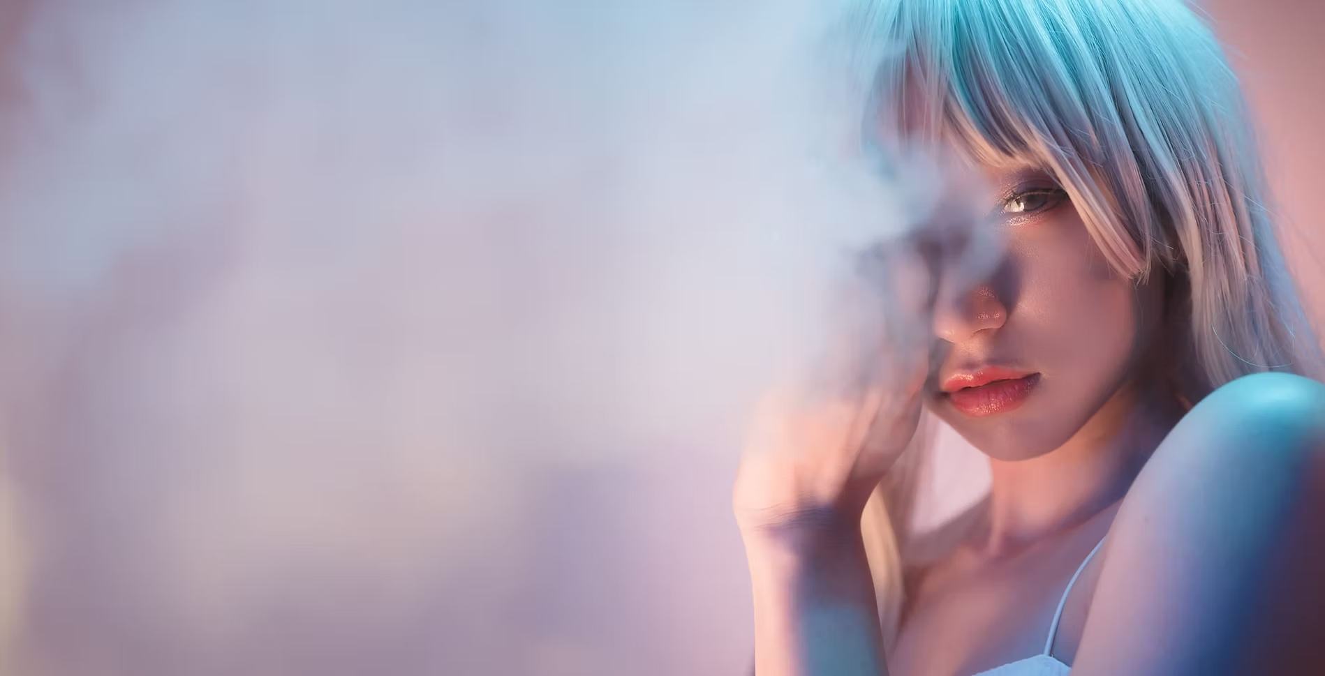A woman with light purple hair, wearing a white top, touching her face with her hand, looking into the camera with a serious expression, in a colorful, softly lit setting.