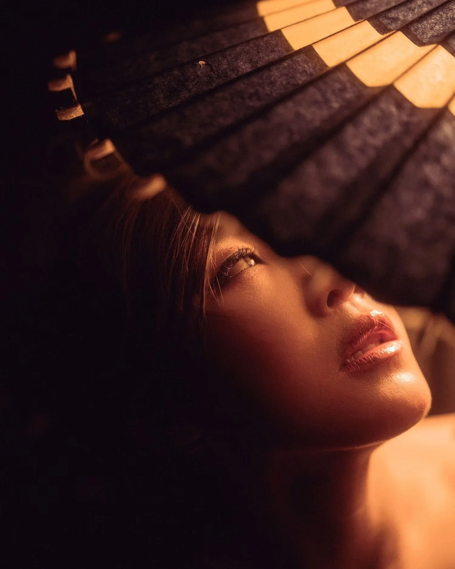 Close-up of a woman's face illuminated by a warm, soft light, with her eyes closed and smiling slightly, surrounded by dark shadows.