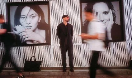 Man standing between two large black-and-white portrait photographs of women at an indoor gallery or exhibition.
