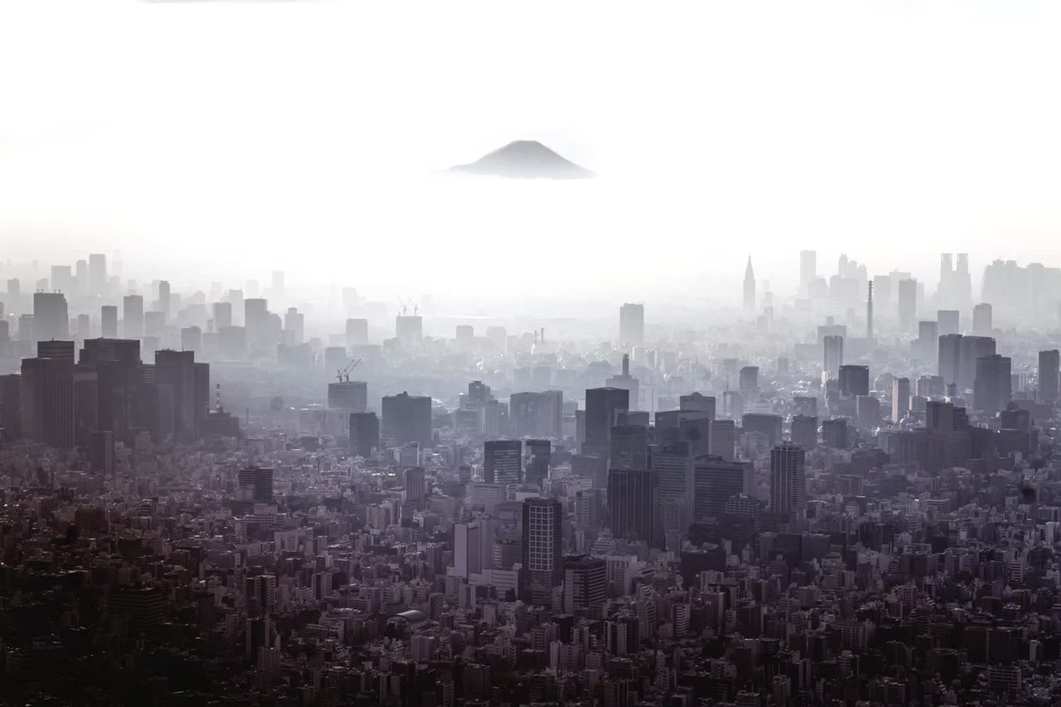 A black and white cityscape featuring numerous skyscrapers with a mountain in the background, shrouded in a hazy or foggy atmosphere.