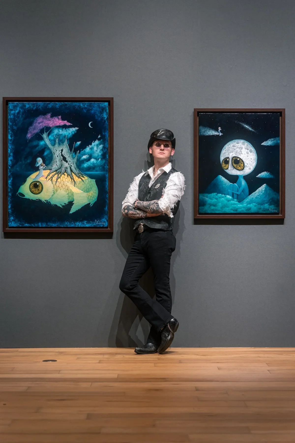 August Vilella
---
Full-length editorial portrait of Spanish surrealist artist August Vilella standing confidently between two of his colourful paintings featuring fantastical creatures with oversized eyes. Photographed at his contemporary art exhibi