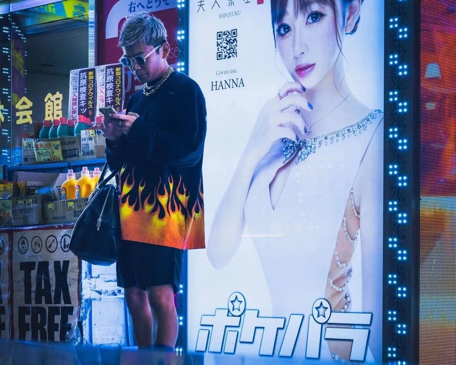A person standing in front of a brightly-lit advertisement in Kabukicho, with a large image of a woman.