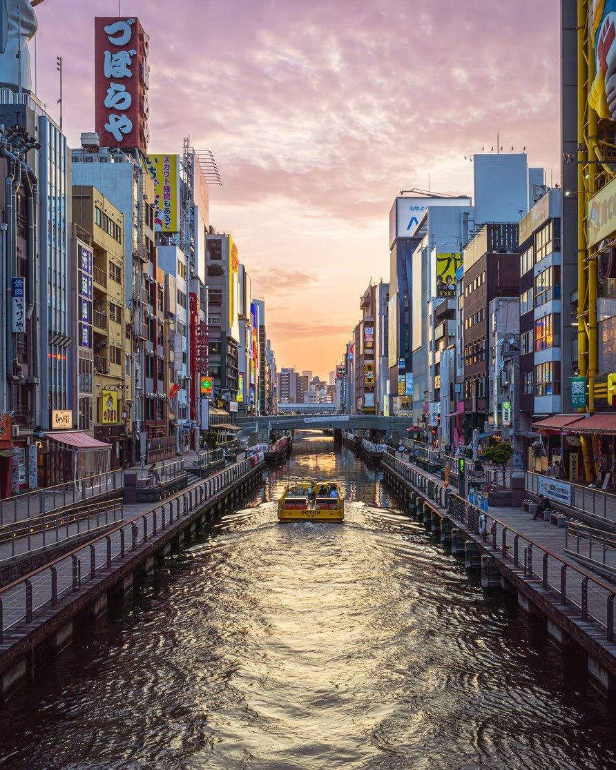 City canal with buildings on both sides, a boat in the center, and a sunset sky overhead.
