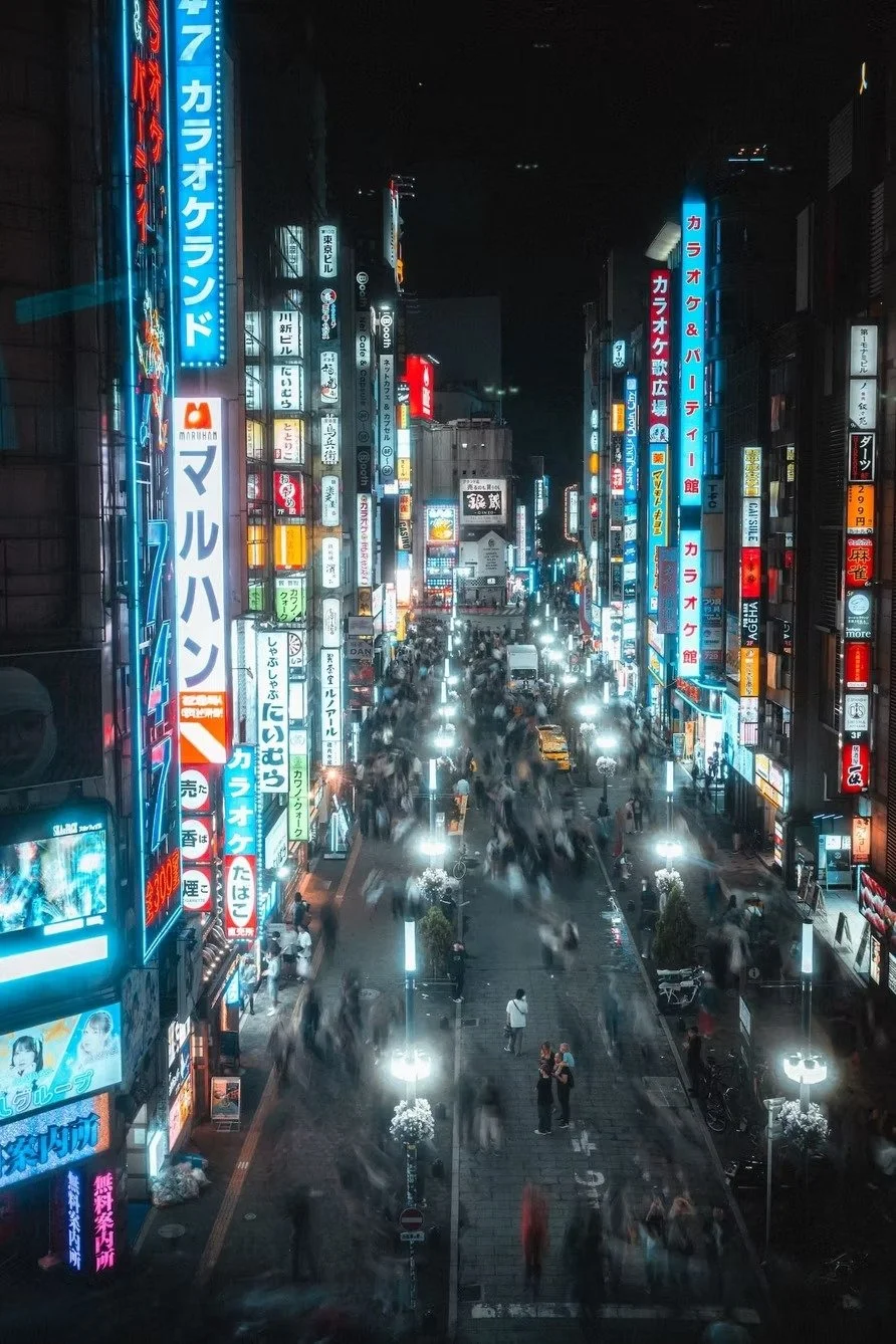 Night view of a busy city street in Japan with bright neon signs in Japanese, crowded pedestrians, and illuminated streetlights.