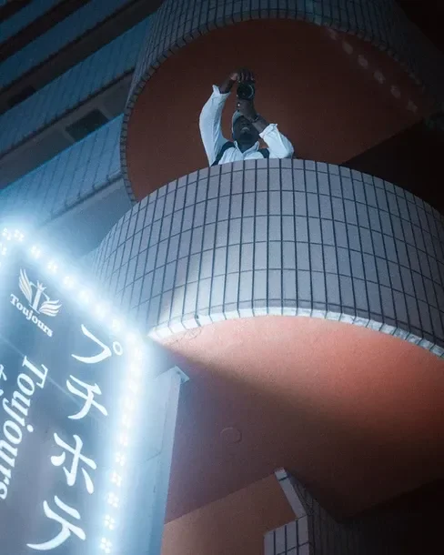 A street shot showcasing a person at a height with neon signs glowing around. Captured as part of the Tekumi Photowalks street photography
