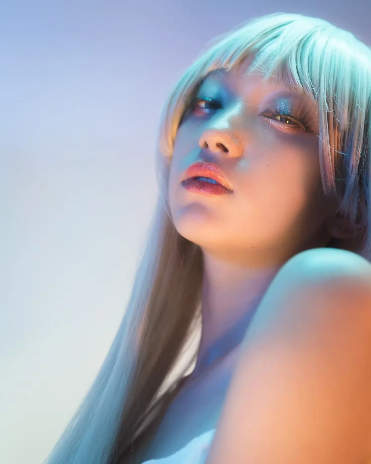 A close-up of a person's face with platinum blonde hair, eye makeup, and slightly open lips. The person has a relaxed and confident expression.
