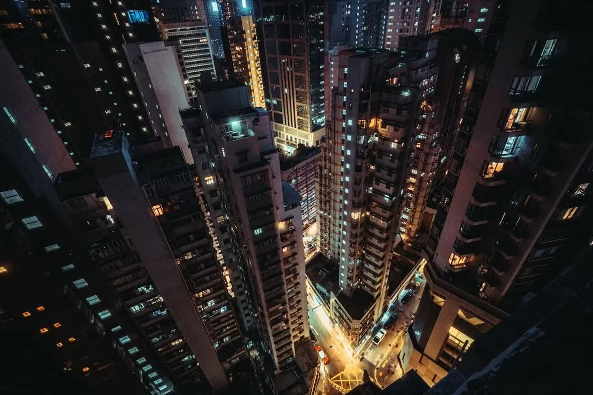 Nighttime Hong Kong view of a dense city with tall skyscrapers, lit windows, and illuminated streets.