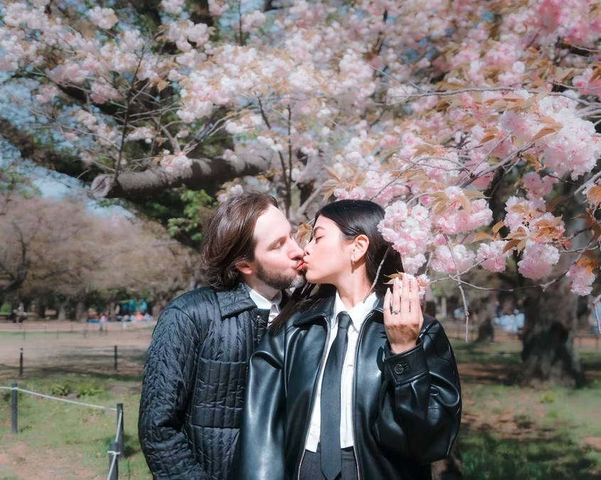 A couple kisses under the blooming cherry blossoms in a Tokyo park. The vibrant pink flowers and sunny weather create a romantic and peaceful atmosphere.