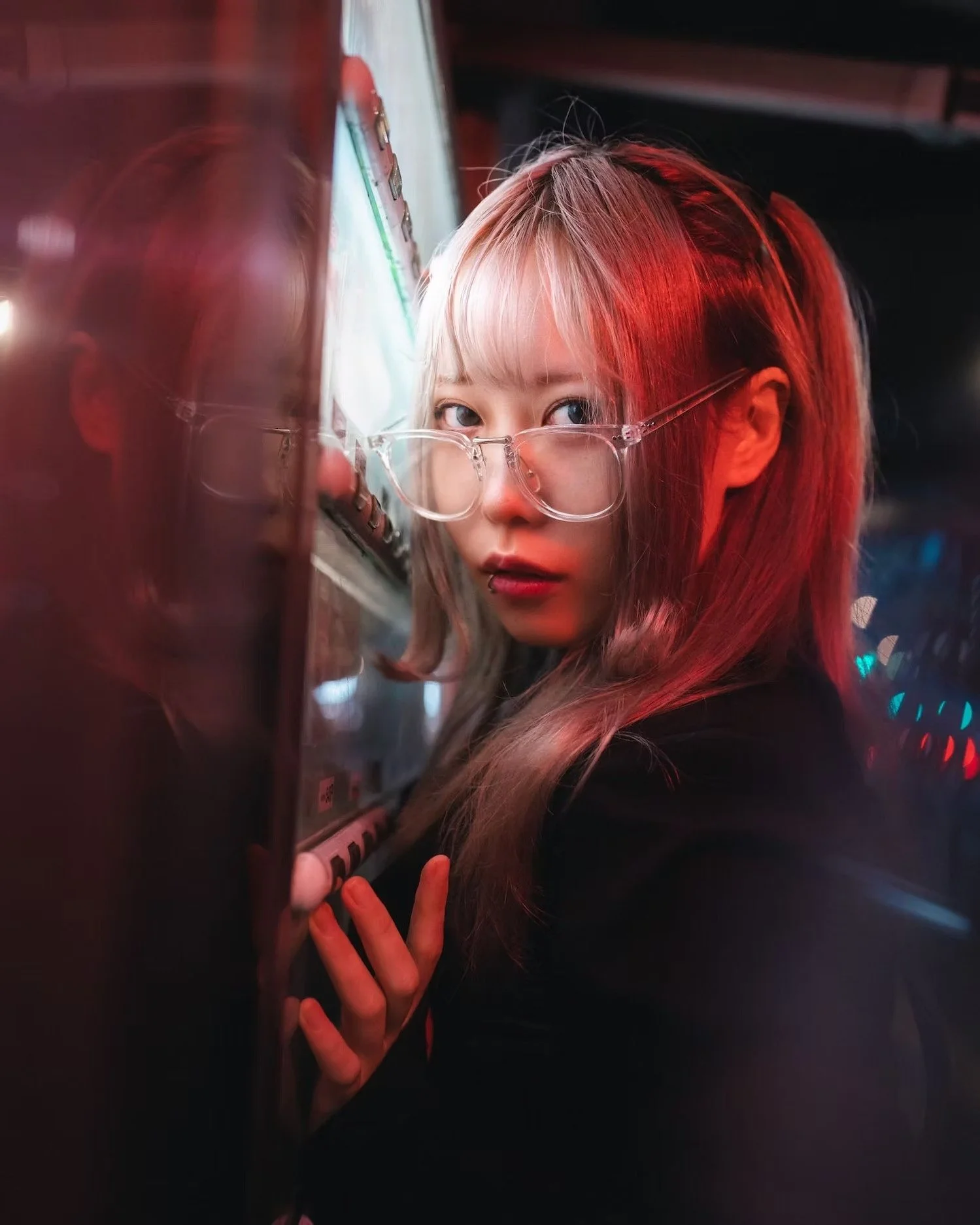 A person with long blonde hair, wearing glasses, looking over the vending machine, illuminated by red and blue lights.