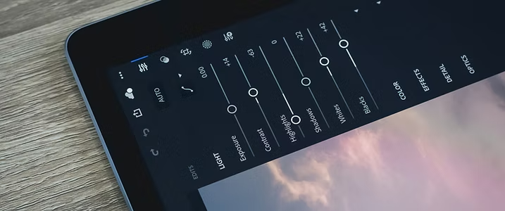 A smartphone screen displaying photo editing settings, including brightness, contrast, highlights, shadows, temperature, tint, color, effects, and vignette, on a wooden surface.