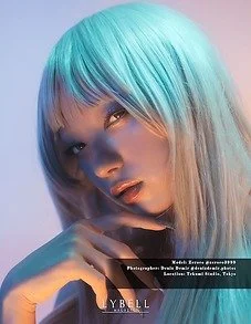 Close-up portrait of a woman with light blue and platinum blonde hair, posing with her hand near her face.