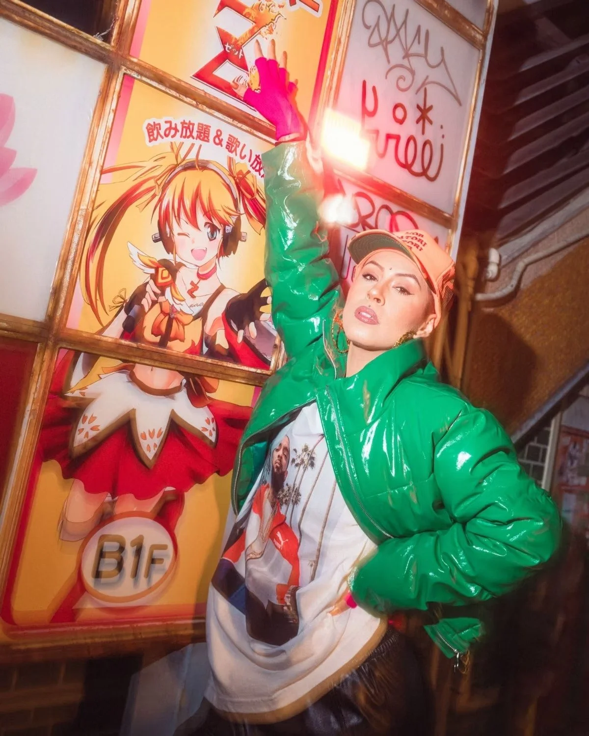 A woman strikes a bold pose in front of colorful anime posters on a Tokyo street, wearing a vibrant green jacket and a graphic shirt. The dynamic lighting and motion blur add energy and character to the scene. Street photography by Deniz Demir.