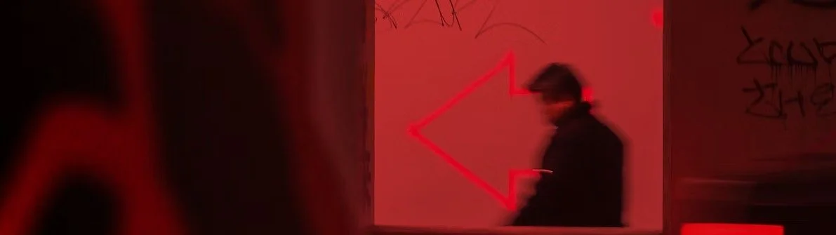 A person walking past a graffiti-covered wall illuminated with red lighting.