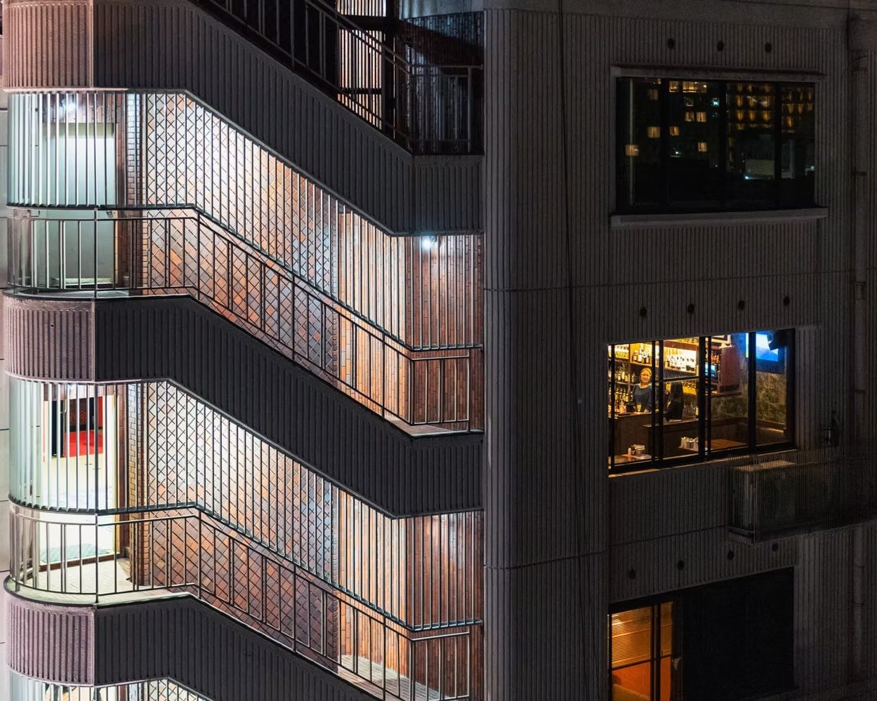 Night view of a multi-story building showing external staircases with metal railings and lit windows, including a visible bar or restaurant on one of the floors.