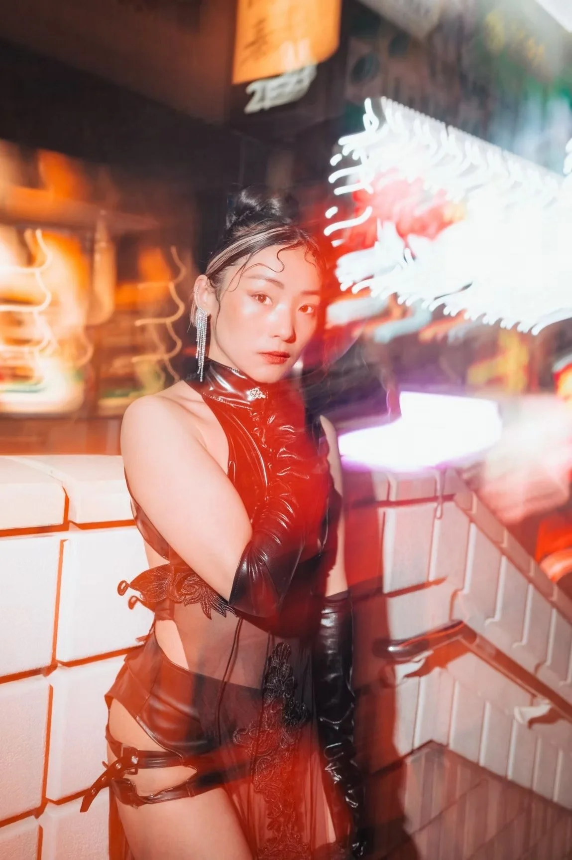 A woman poses in a bold red outfit against a vibrant city backdrop with neon lights. The motion blur creates a sense of movement and energy, capturing the dynamic atmosphere of Tokyo at night. Street photography by Deniz Demir.
