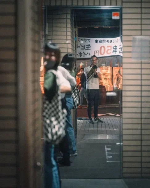 A photographer capturing a moment through a narrow alley, part of the Tekumi Photowalks street photography workshop in Tokyo.