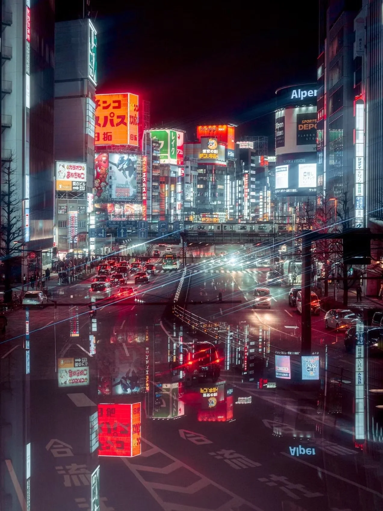 Nighttime cityscape of a busy urban street in Japan with illuminated signs, billboards, and traffic reflections on the wet road.
