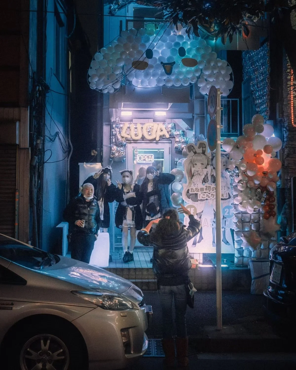 People in costumes taking photos in front of a decorated storefront with balloons and signs at night around Kanda area Tokyo.
