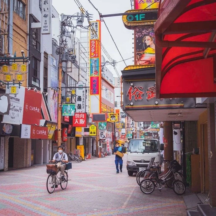 A cyclist riding through a colorful Osaka street with vibrant signs, captured during street and portrait photography.