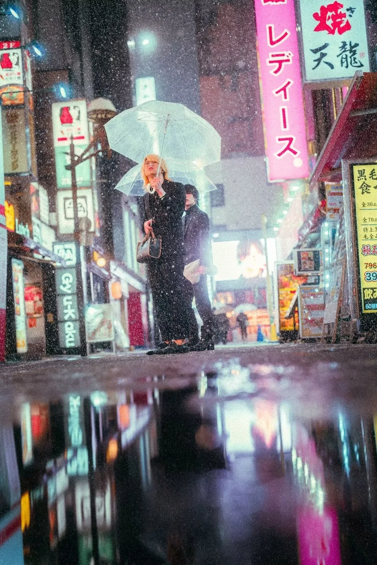 A host standing on a city street at night holding a transparent umbrella during rain, with neon signs and buildings in an urban setting in Kabukicho