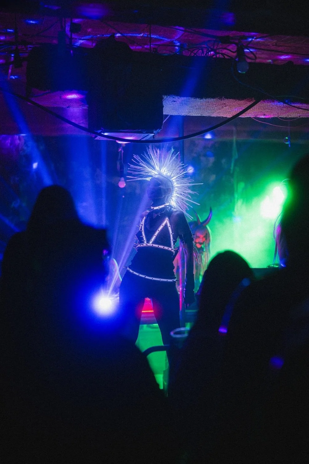 Bondage Ball event in the Ohjo building in Kabukichi, Shinjuku, a person with a spiked halo and glowing costume performing in a dark, neon-lit club or rave with silhouettes of other people watching.